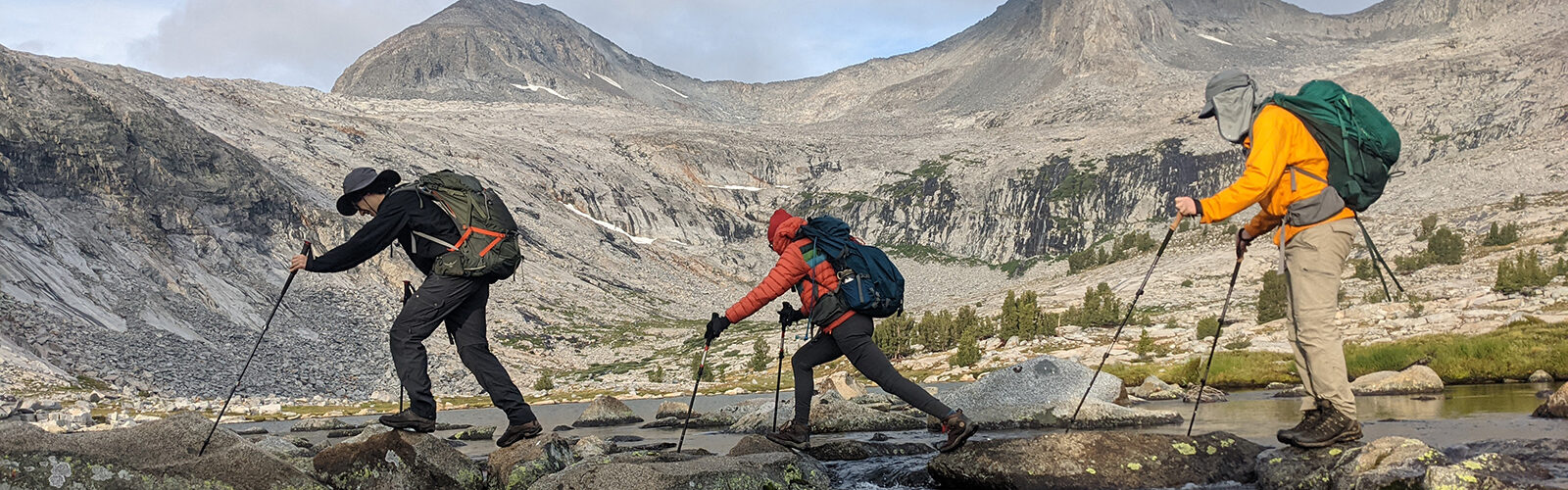 three mountain climbers traversing a rocky creek bed with backpacks on